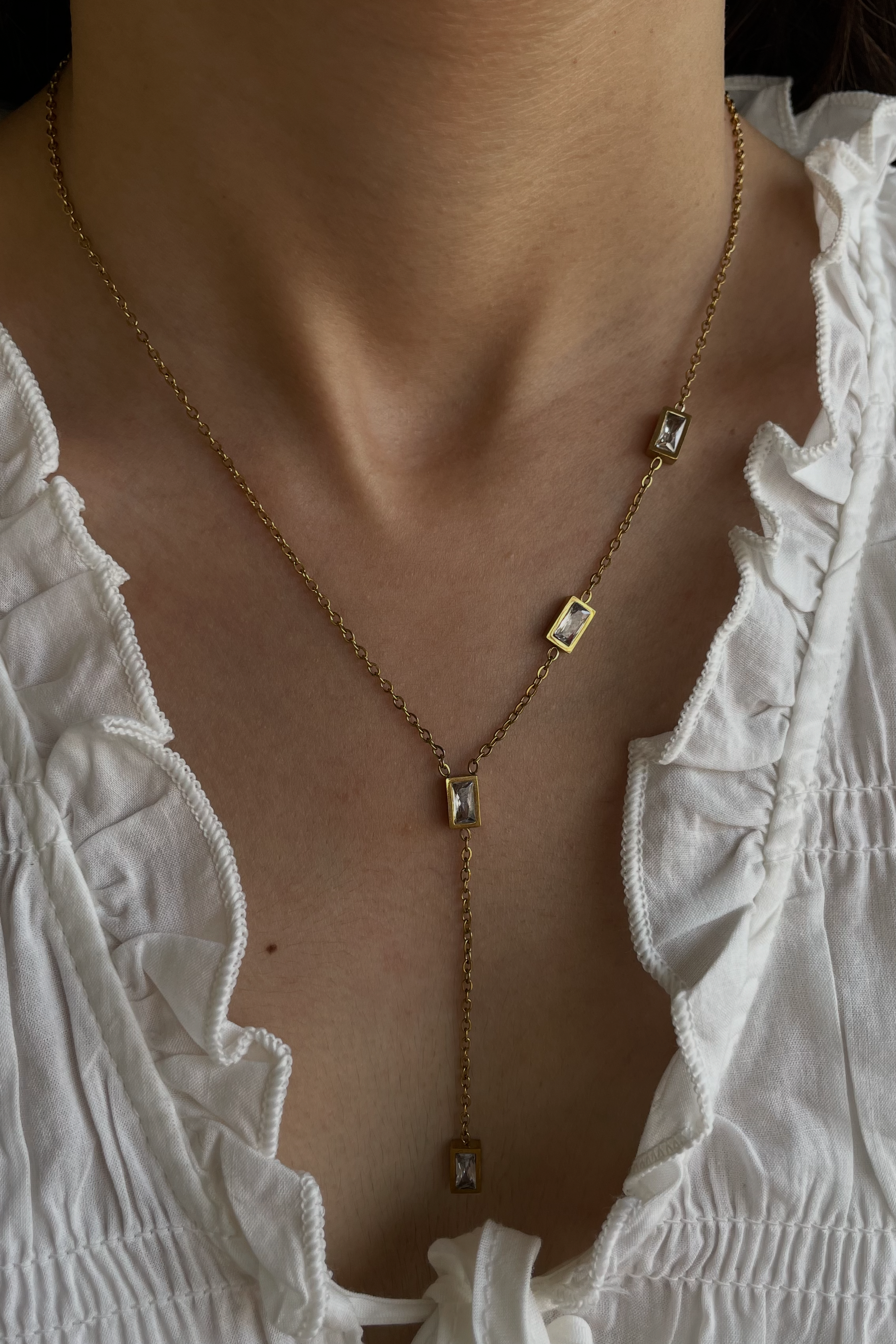 Gold necklace with square pendants worn by a person in a white top.