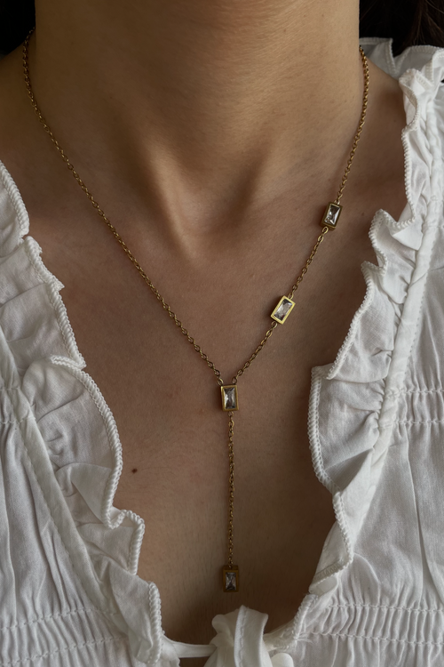 Gold necklace with square pendants worn by a person in a white top.