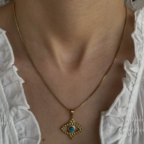 Gold necklace with a blue pendant worn by a person in a white lace top.